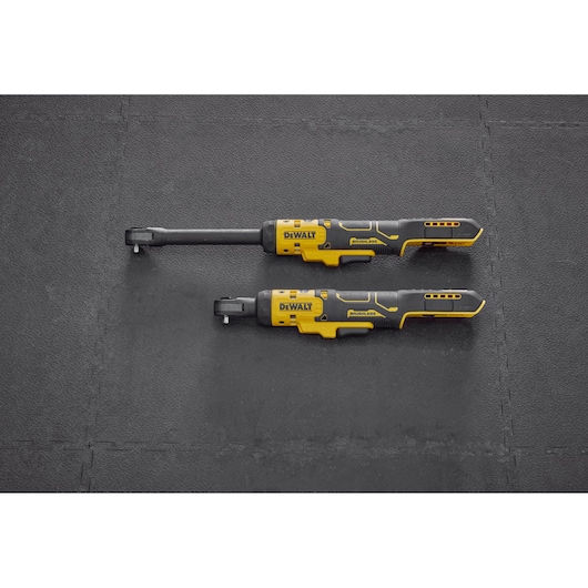 Two DEWALT cordless ratchet tools, one with a longer neck and one with a standard neck, are placed side by side on a black textured surface. Both tools feature yellow and black color schemes and ergonomic handles.