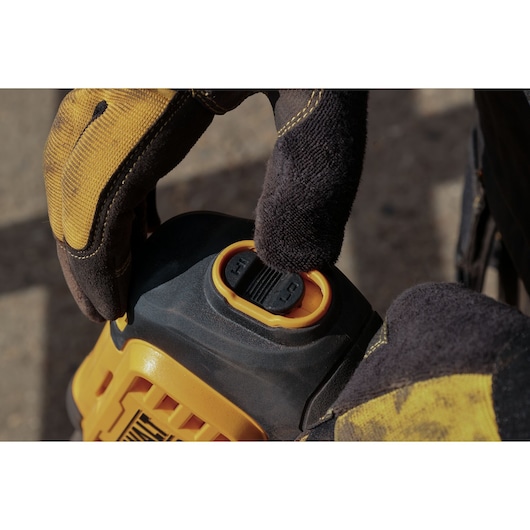 A close-up image of a gloved hand adjusting the control switch on a DEWALT power tool, specifically the DCMPW1000N model. The tool features yellow and black components.